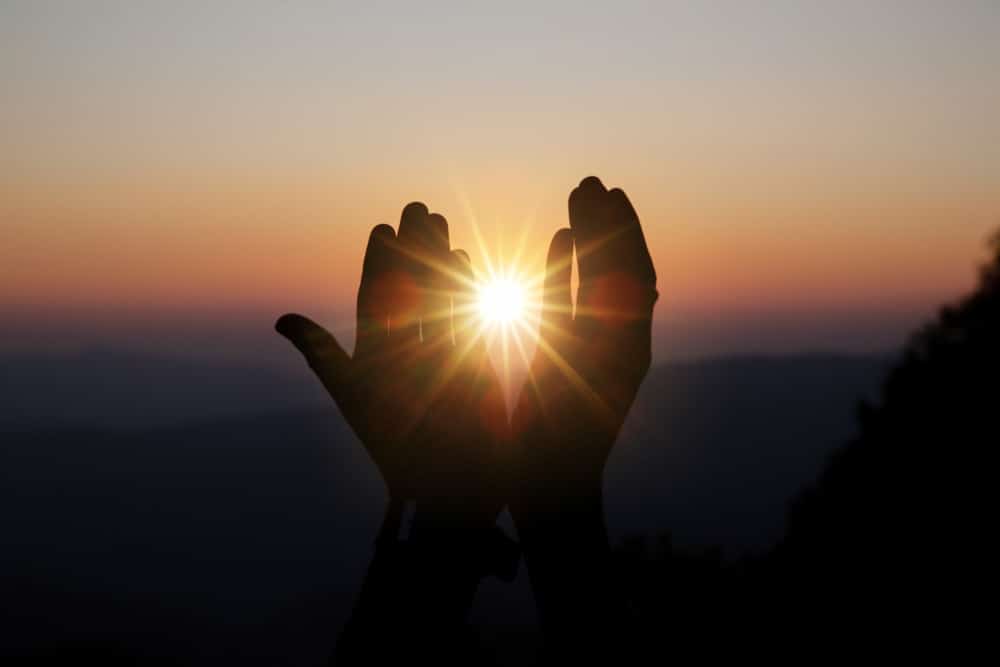 Mains entrouvertes laissant apercevoir le soleil se couchant